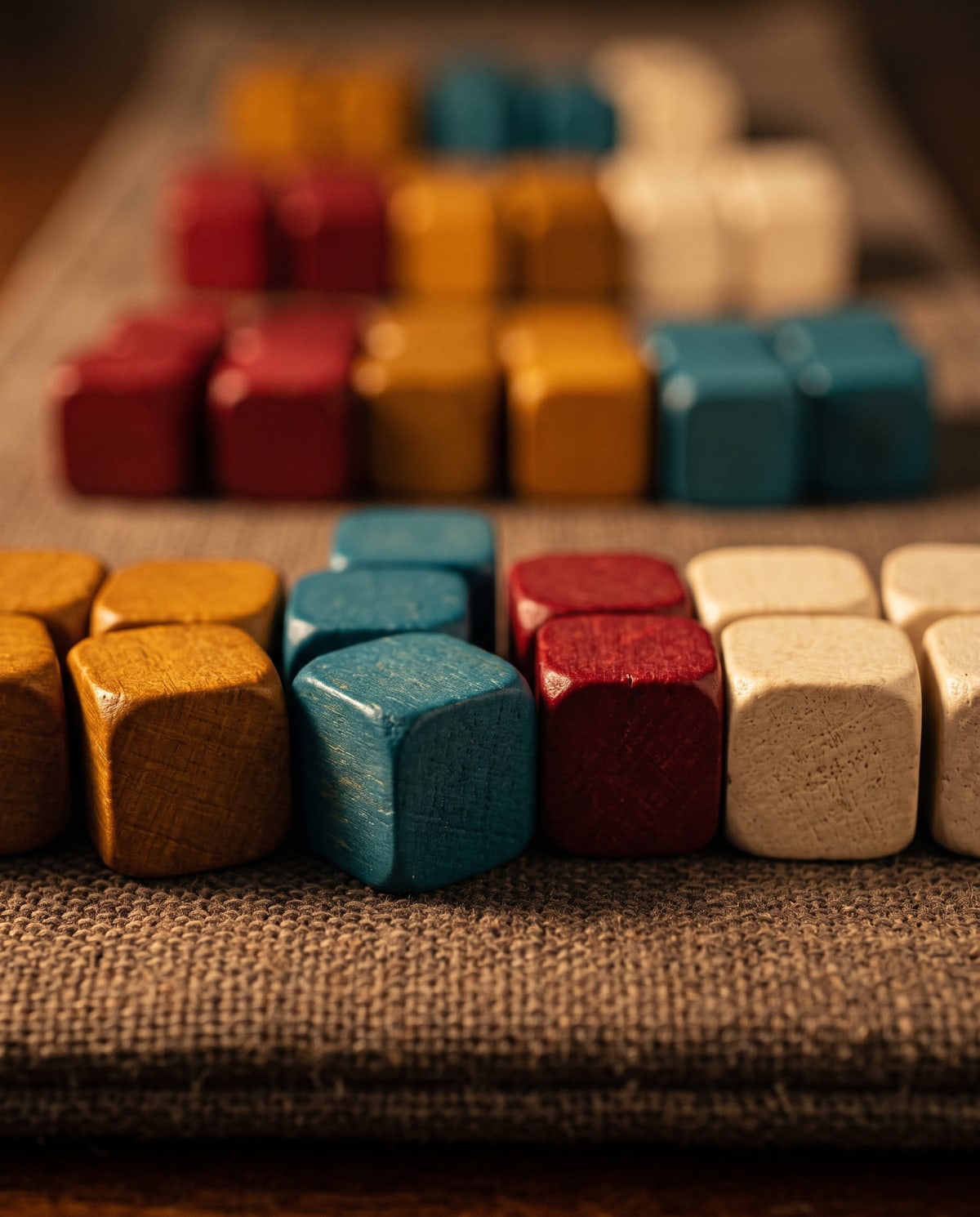 Small wooden cubes in amber, teal, deep red and cream, sorted into rows by colour on a linen-finish supply strip