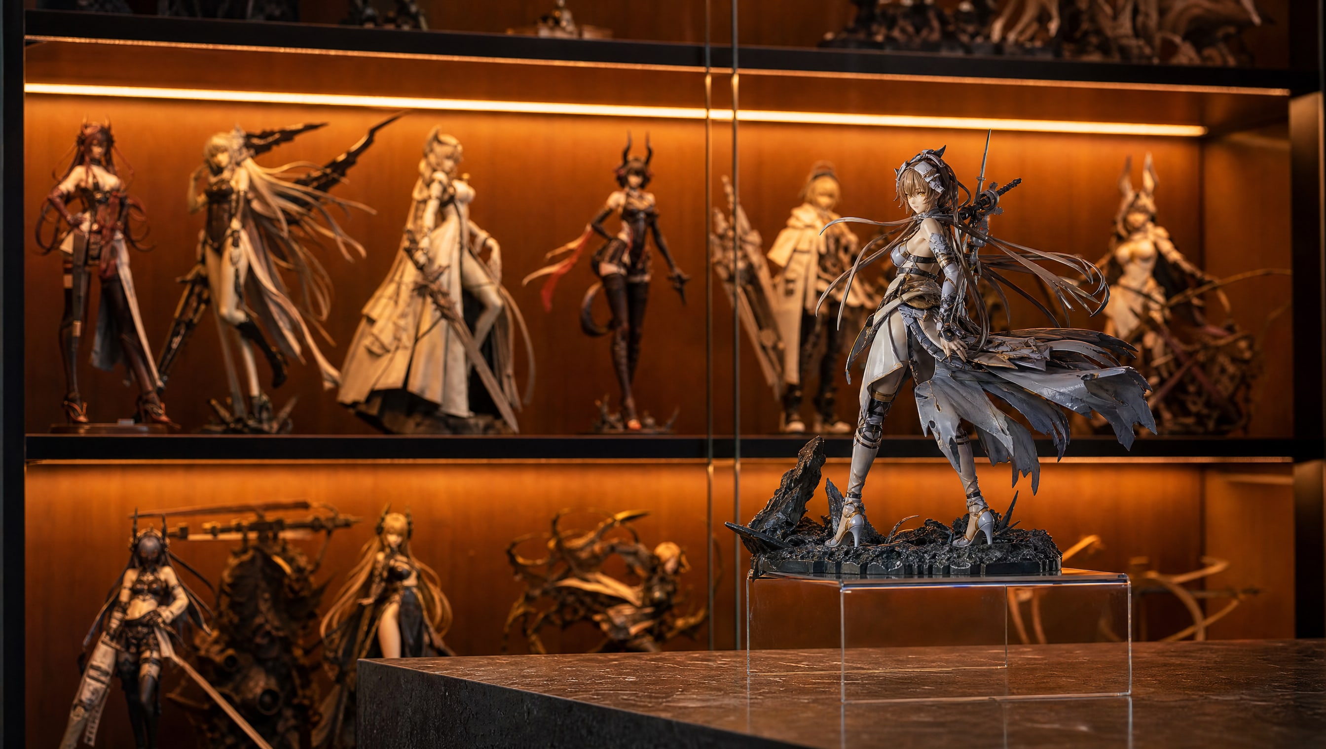A lit shelf of collector figures in warm gallery light, one figure standing forward on a riser.