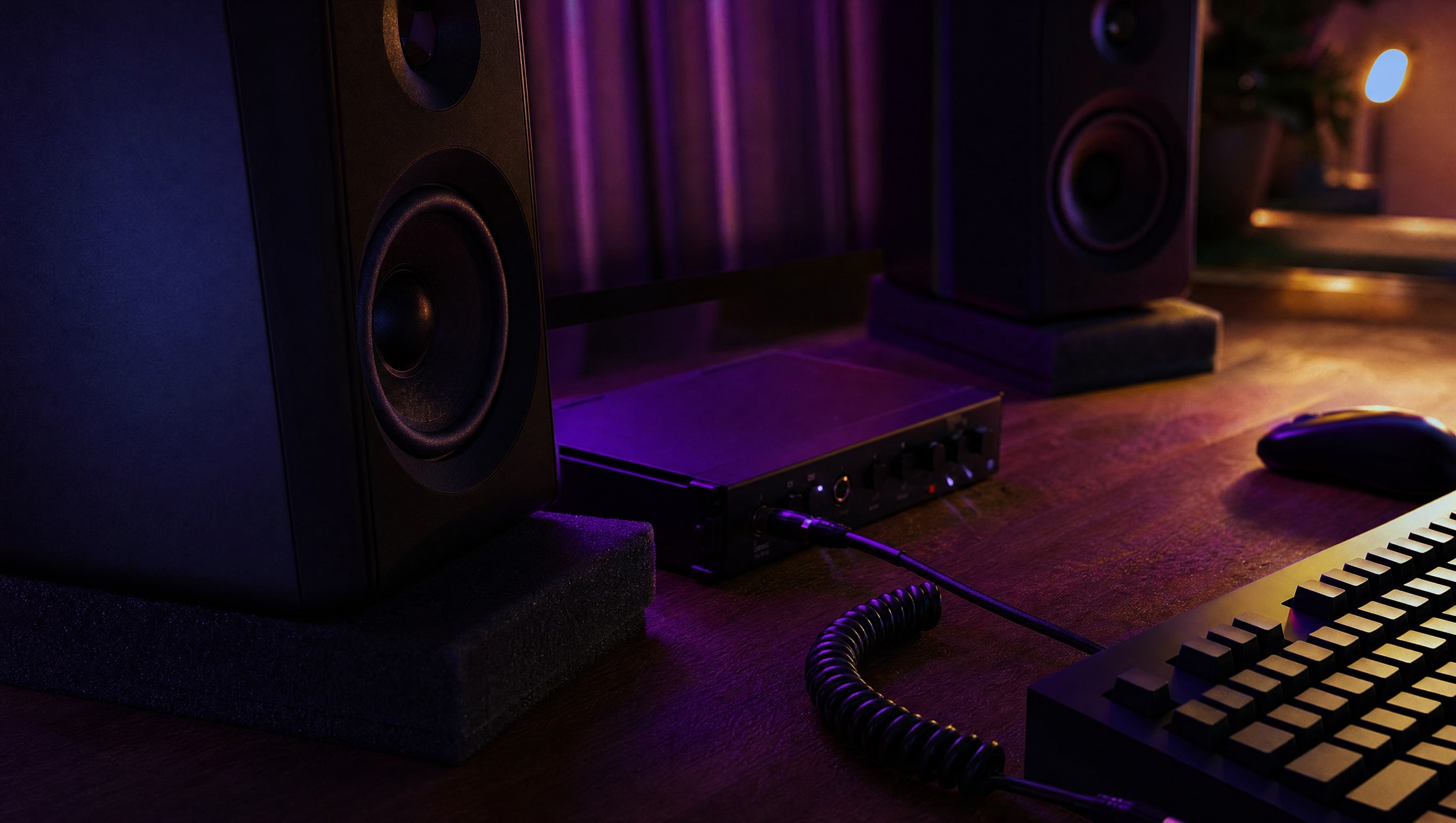 A desk at night: two speakers, an interface, a coiled cable and a foam isolation pad.