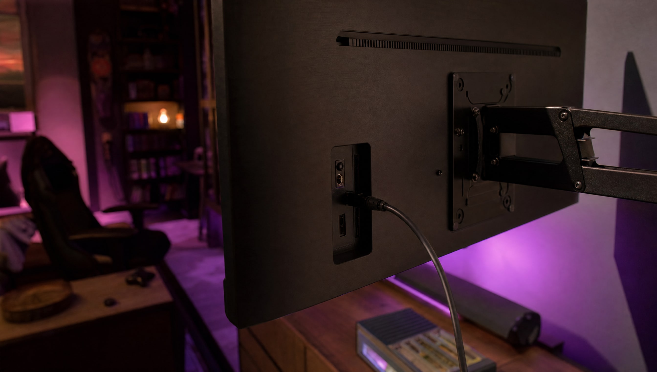 The rear panel of a wall-mounted television, ports in a recess, one cable seated.